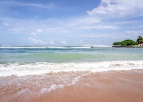 Serene view of Weligama Beach with waves gently hitting the shore under a bright sky.